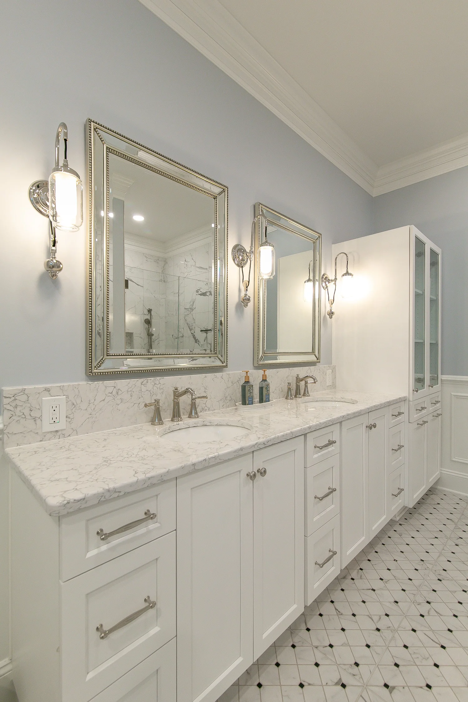 Long custom white double vanity with marble-look countertop, framed mirrors, polished wall sconces, and patterned tile floor in a Ford’s Colony bathroom